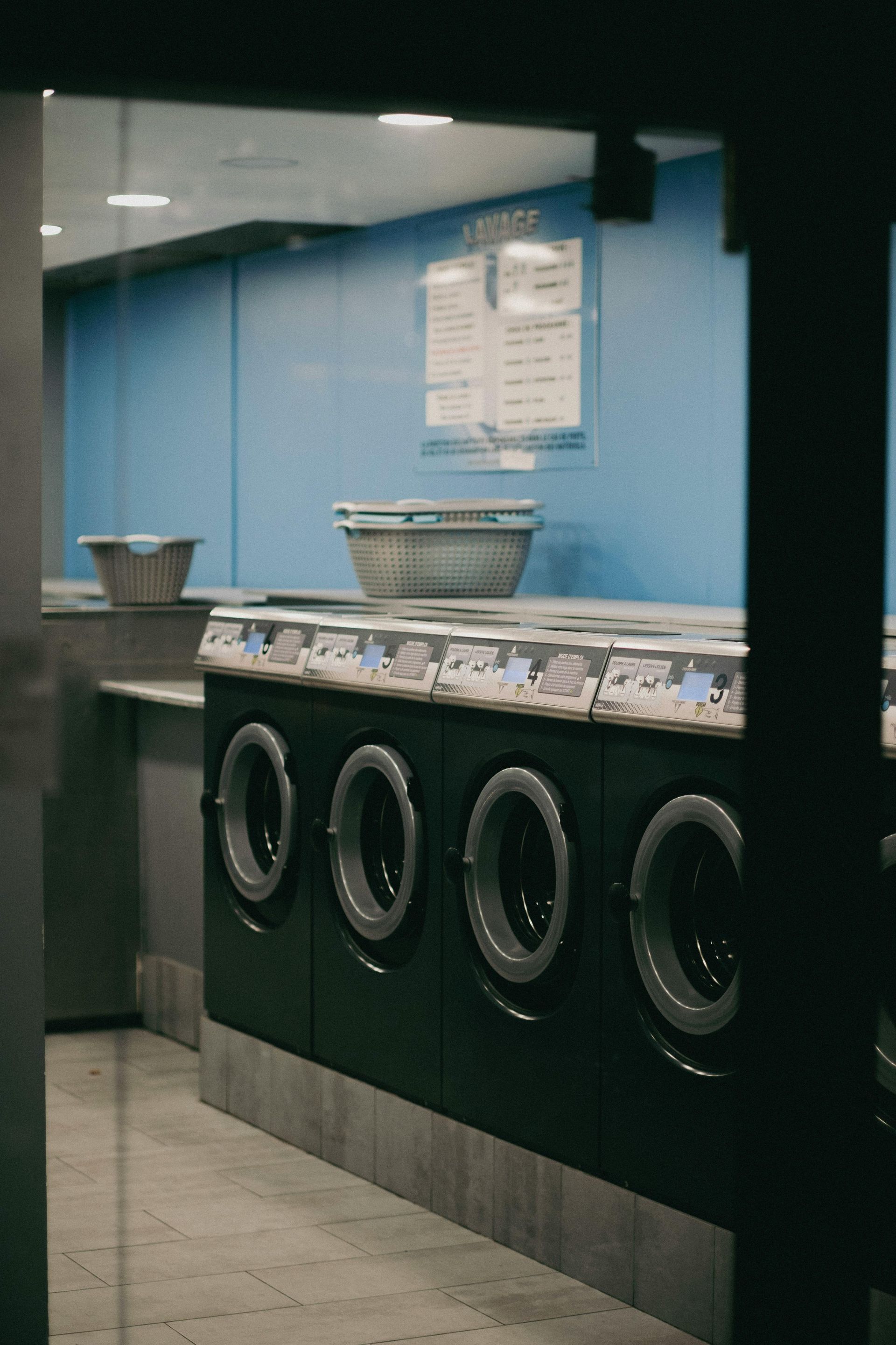 Laundry room with rows of front-loading washers against a blue wall.