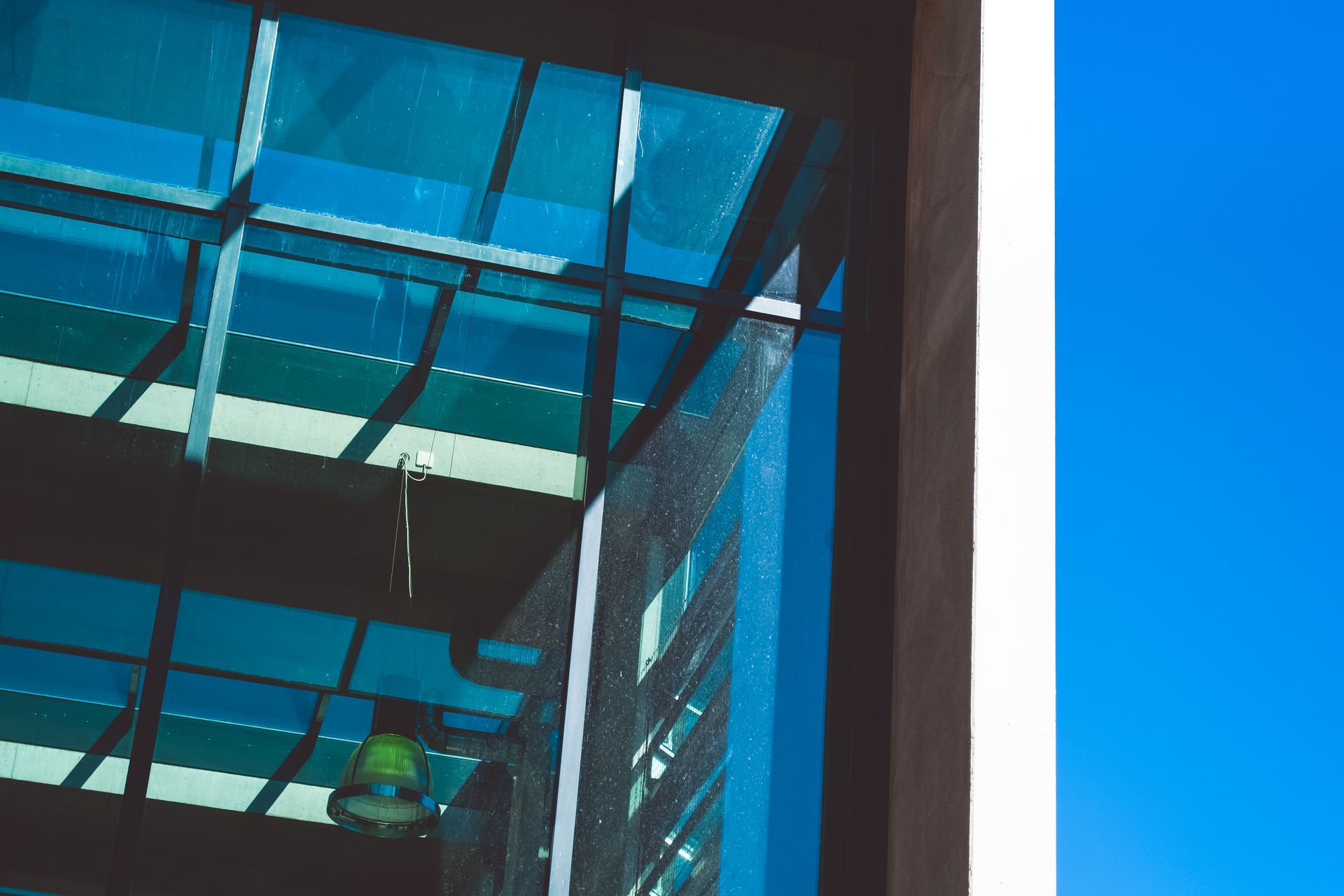 Blue-tinted glass building facade with reflections and a hanging lamp inside