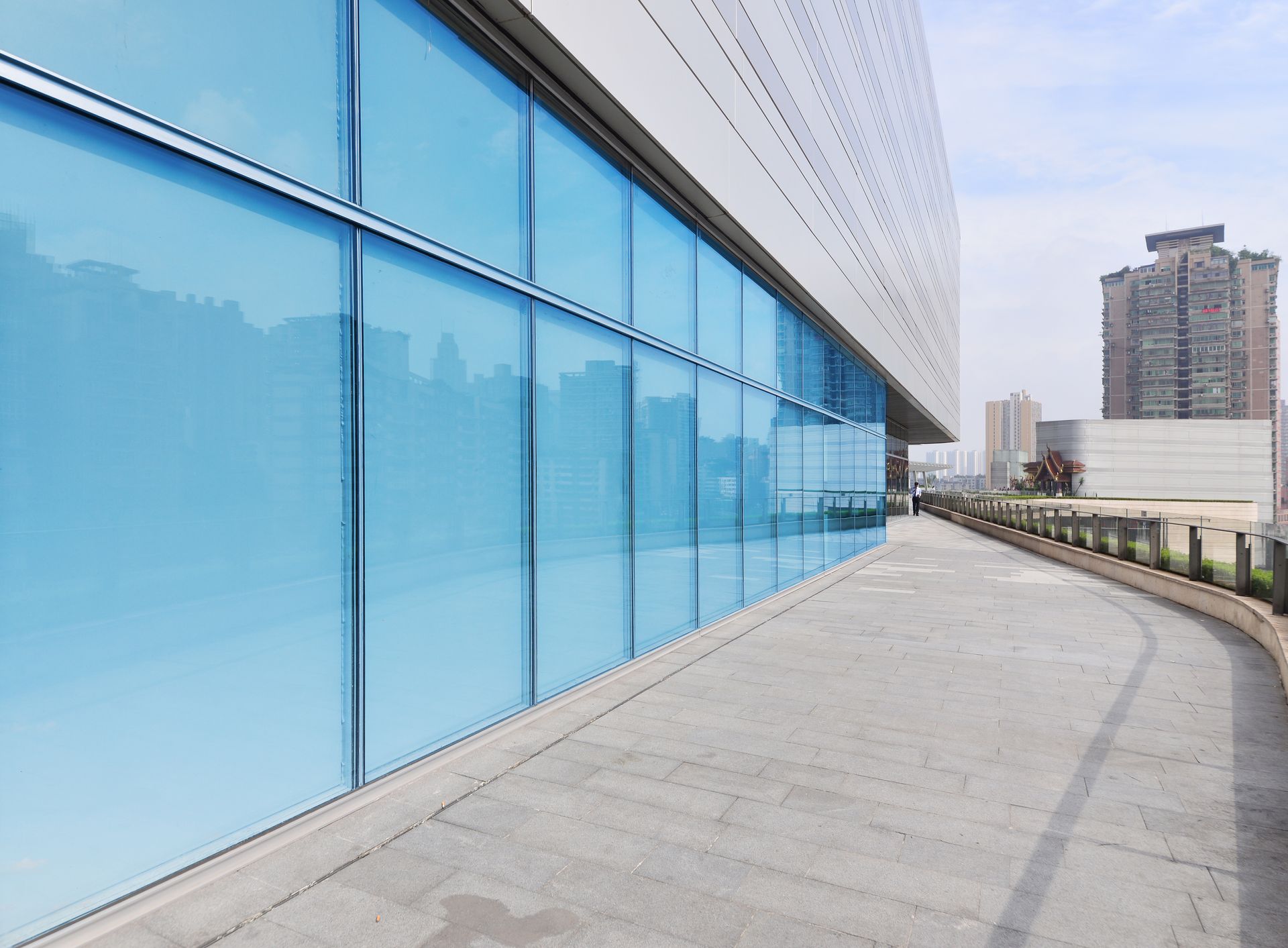 Modern building walkway beside blue glass windows with city skyline in the distance