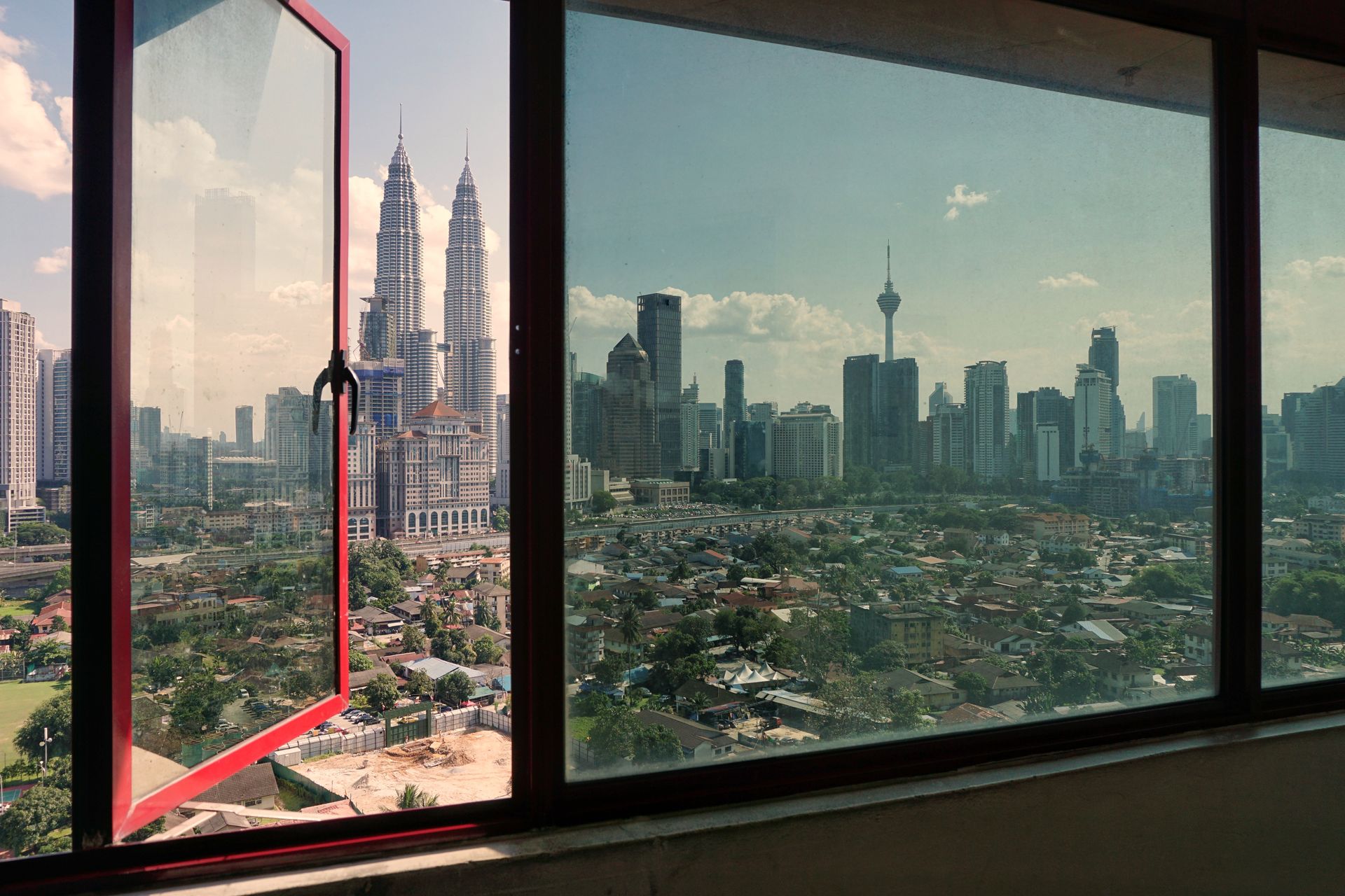 City skyline seen through open window with red frame, including twin towers and a distant TV tower