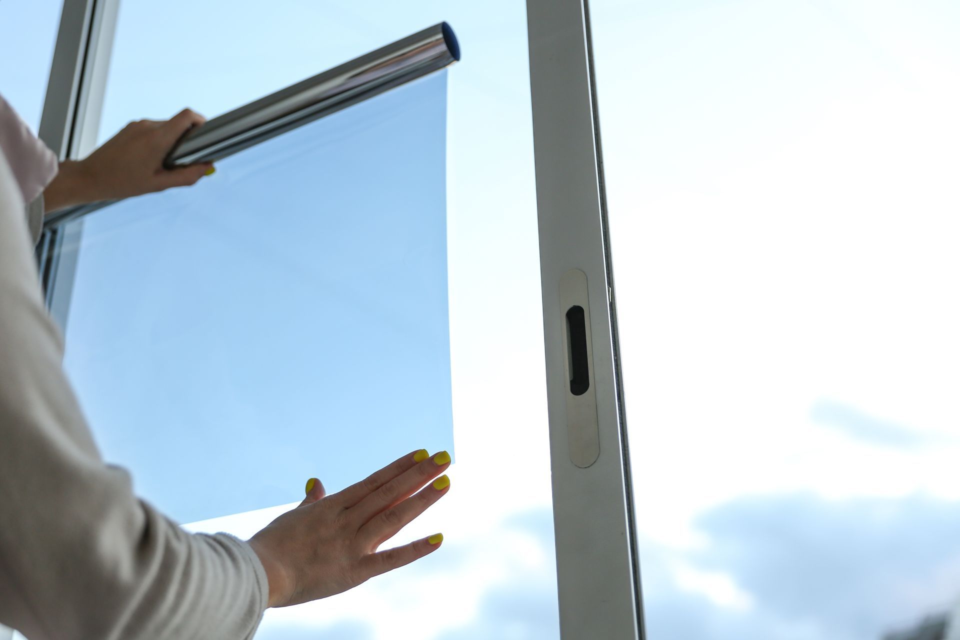 Hands installing a window blind on a bright window with blue sky outside