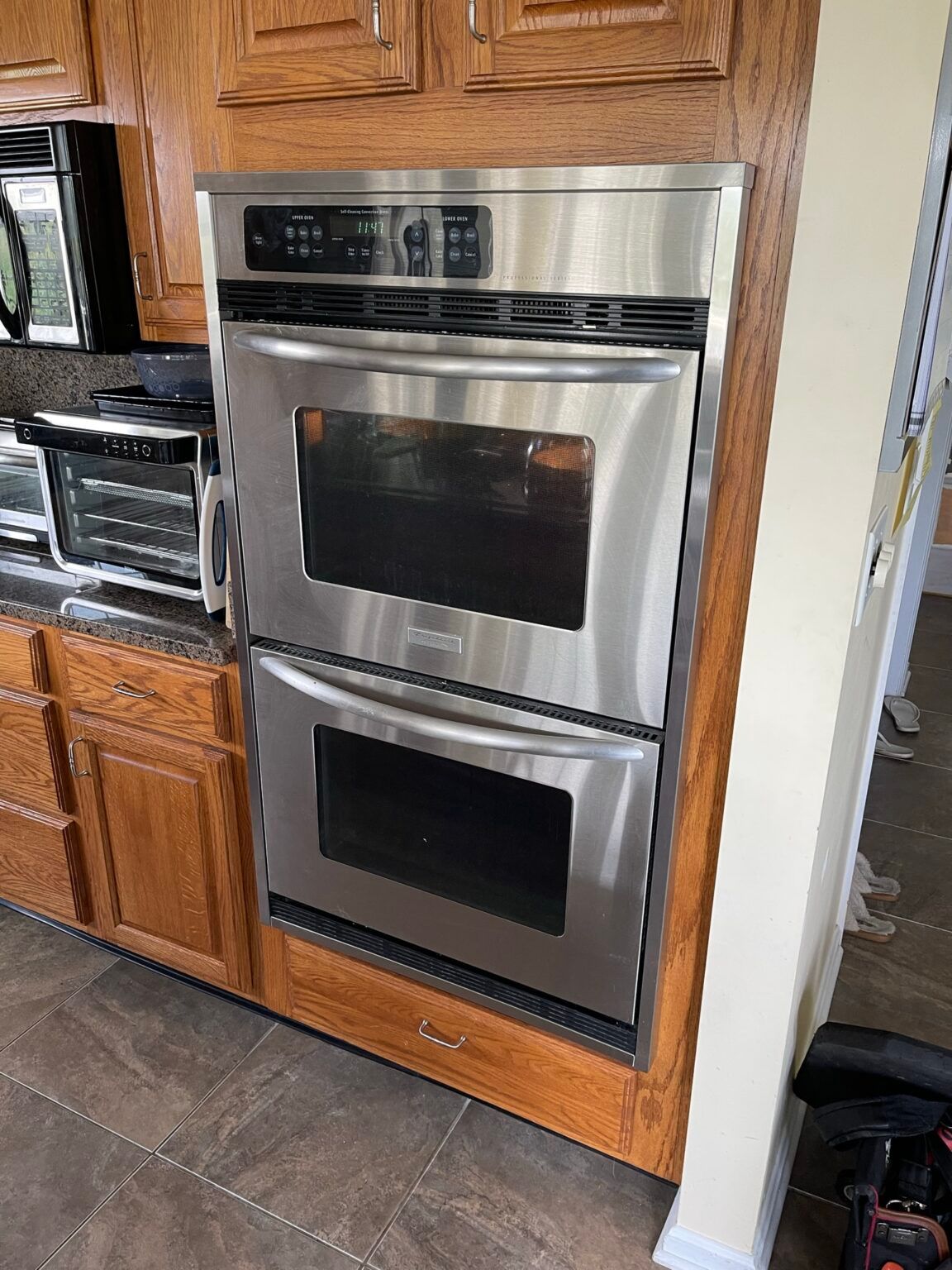 A stainless steel double oven is built into a wooden cabinet in a kitchen.