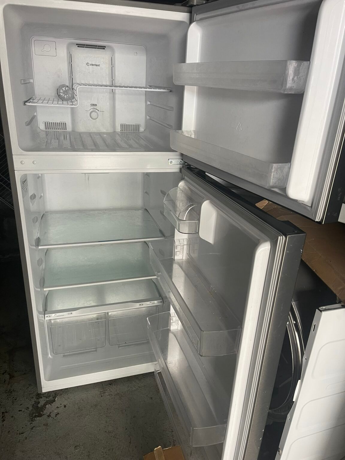 An empty refrigerator with the door open is sitting on the ground.