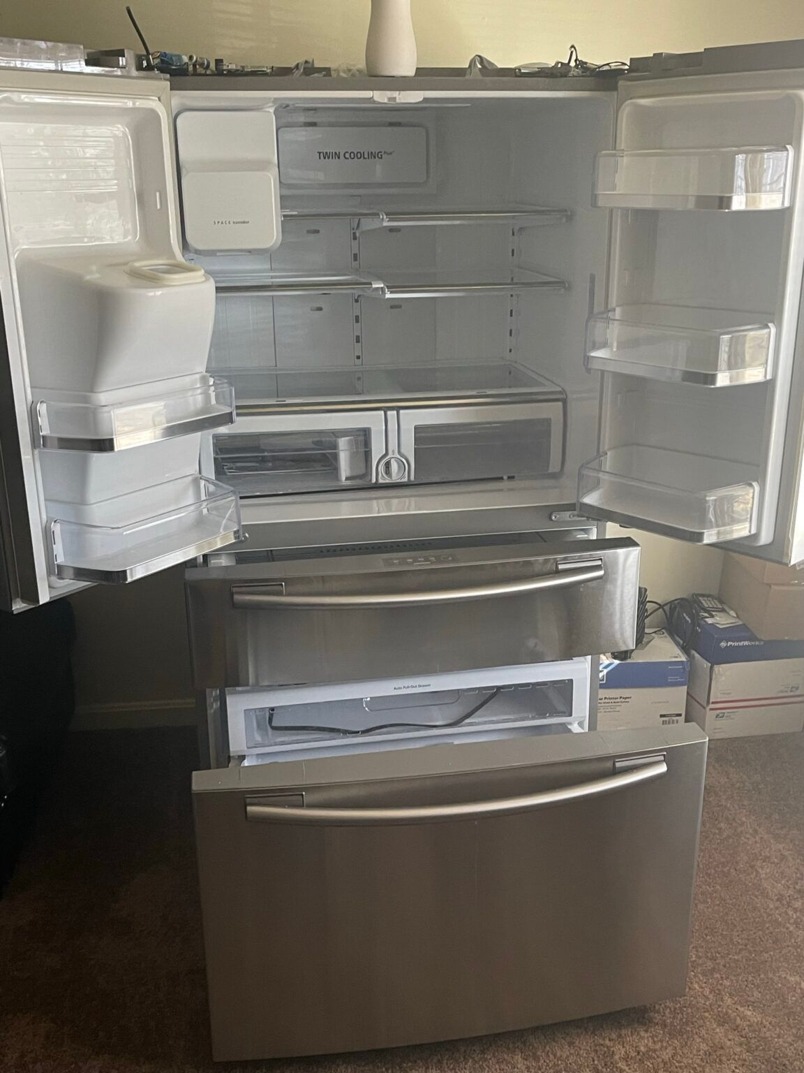 A stainless steel refrigerator with its doors open is sitting on a carpeted floor.