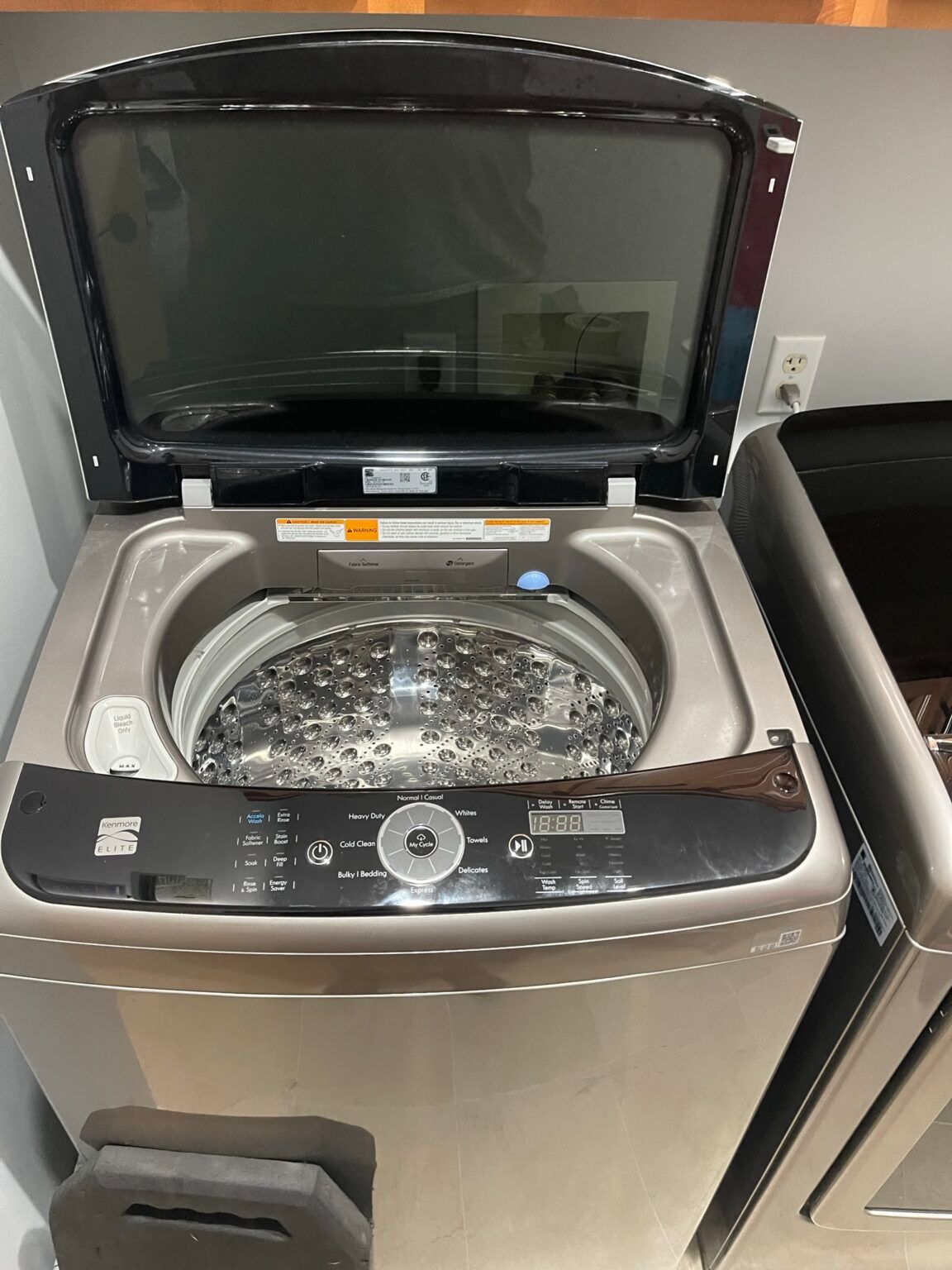 A washing machine with the lid open is sitting in a laundry room.