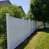 A white vinyl fence is surrounded by trees and bushes in a backyard.