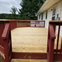 A wooden deck with a red railing is sitting in front of a white house.
