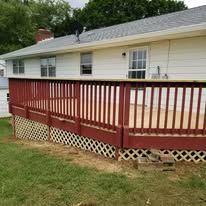 A white house with a red deck and fence in front of it.