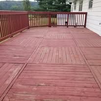 A large red wooden deck with a red railing and a white house in the background.