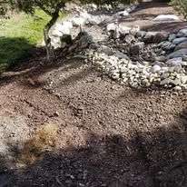 A pile of dirt and rocks in a yard with a tree in the background.