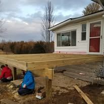 A couple of people are working on a wooden deck in front of a house.