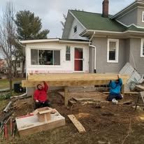 Two men are lifting a wooden deck in front of a house.