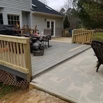 A patio with a wooden railing and a fire pit in front of a house.