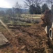 A bulldozer is moving dirt in a field next to a wooden fence.