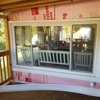 A large window on a porch with a bench and chairs.