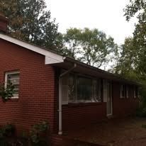A red brick house with a white roof is surrounded by trees.