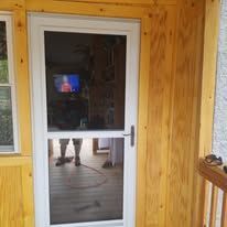 A white door with a glass door is sitting on a wooden porch next to a window.