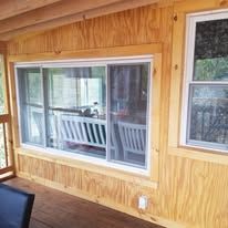 A wooden porch with a large window and a bench.