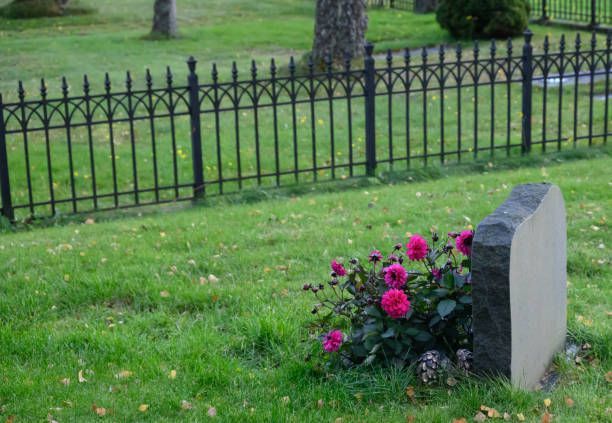 A graveyard with a fence and flowers in the grass.