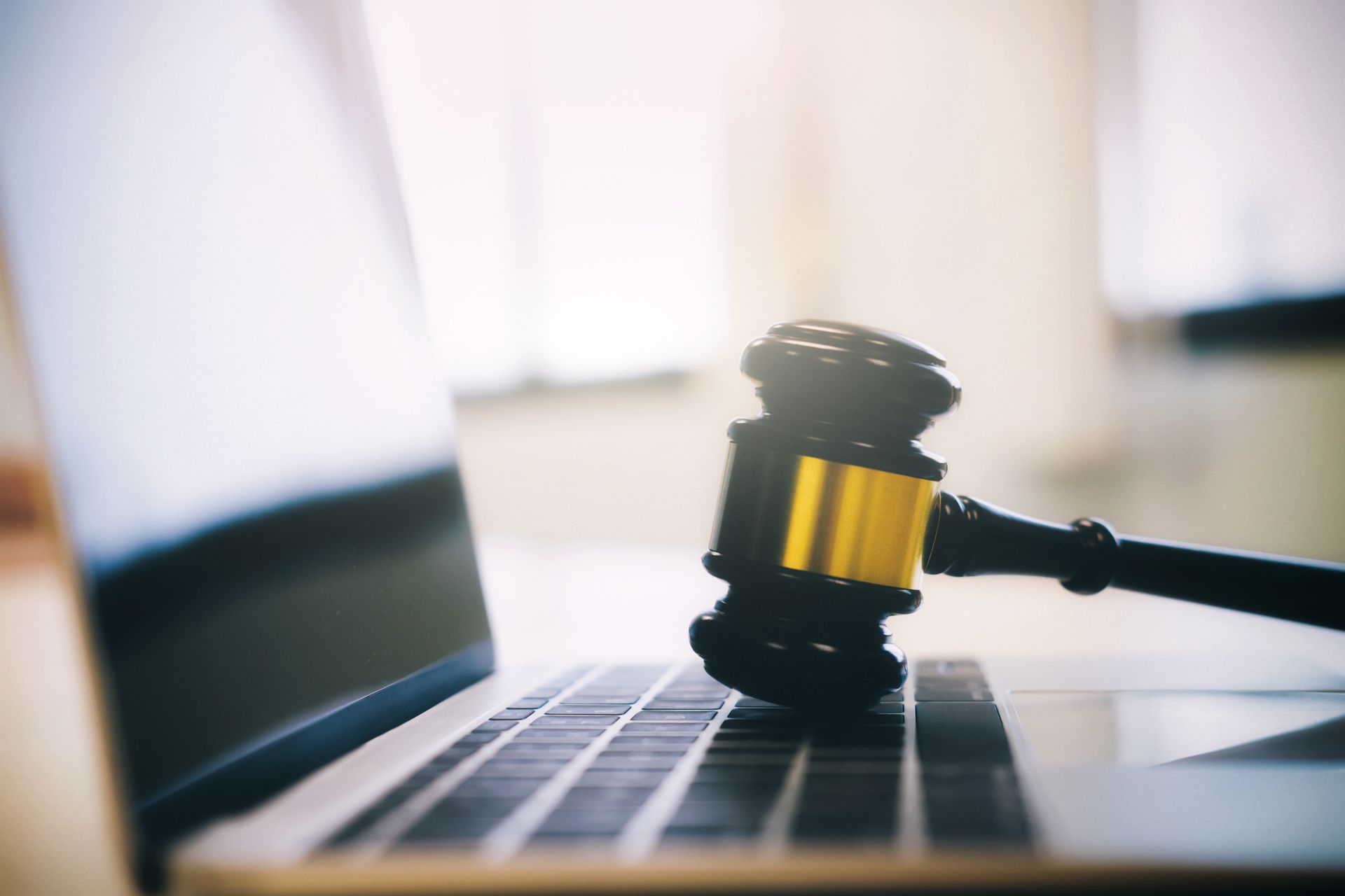 A gavel resting on a laptop keyboard; gold and black with a bright background.