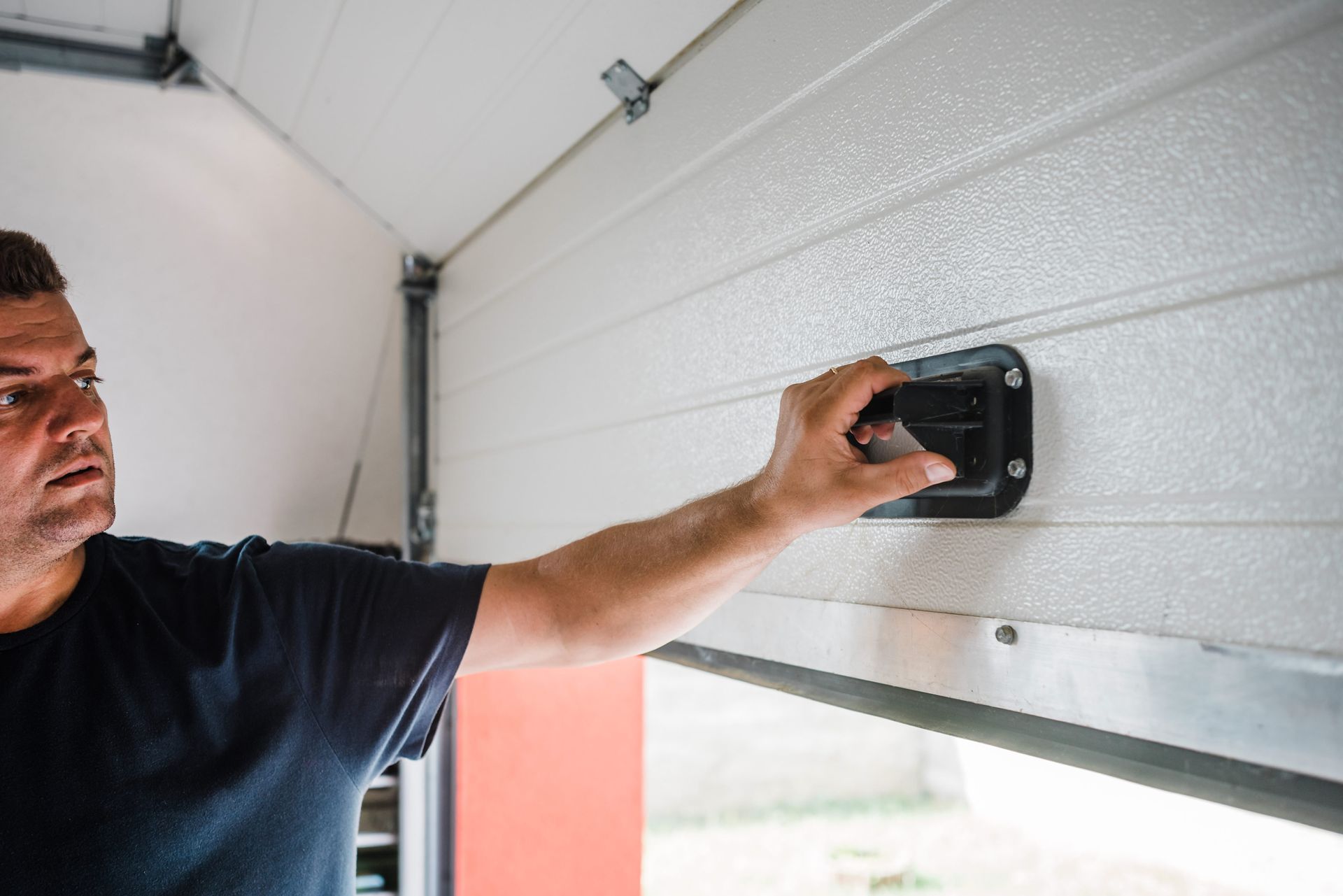 Man working on a garage door, holding a handle, inside a garage.