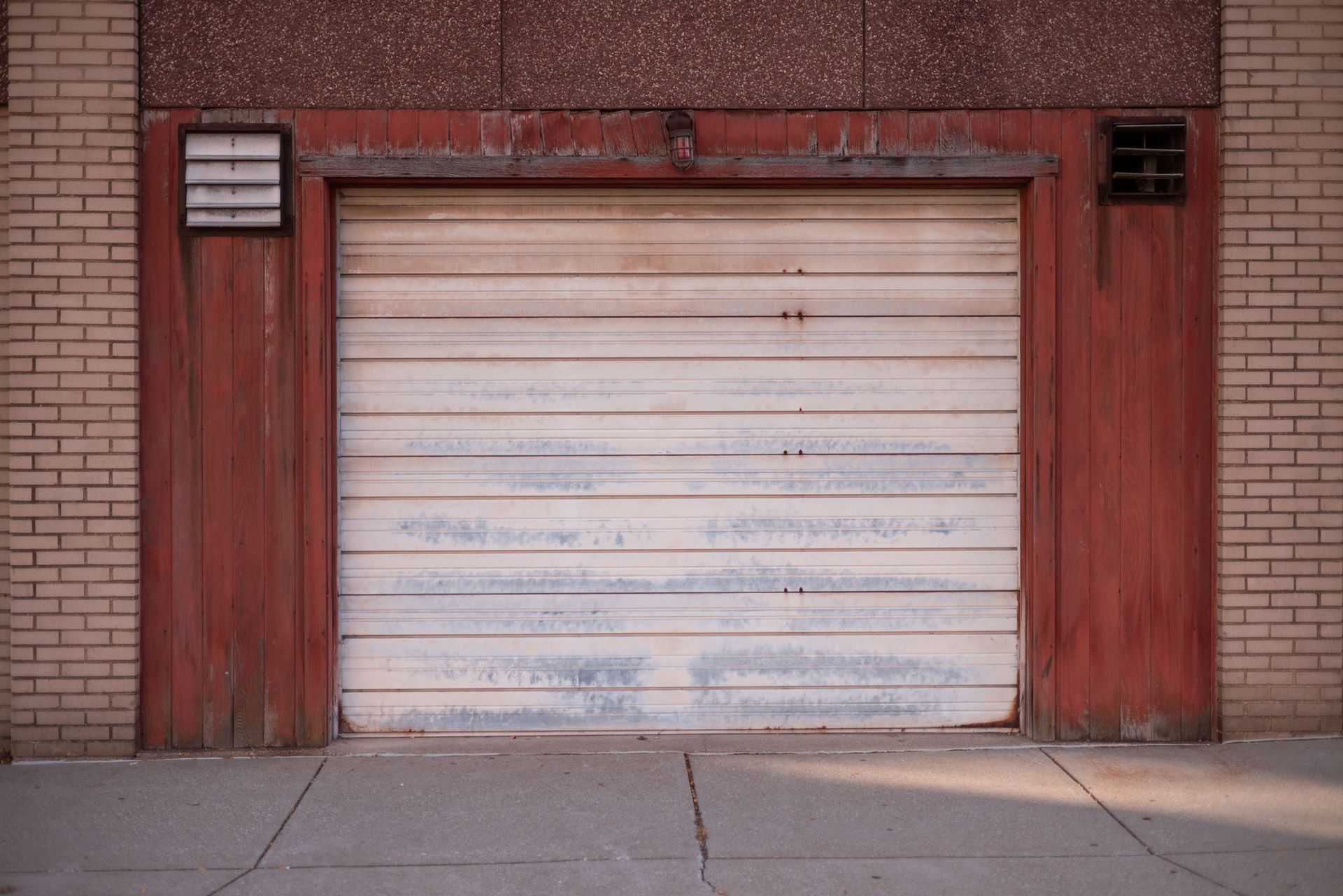 Red-framed garage door on a brick building with two small vents. The door is weathered and white.