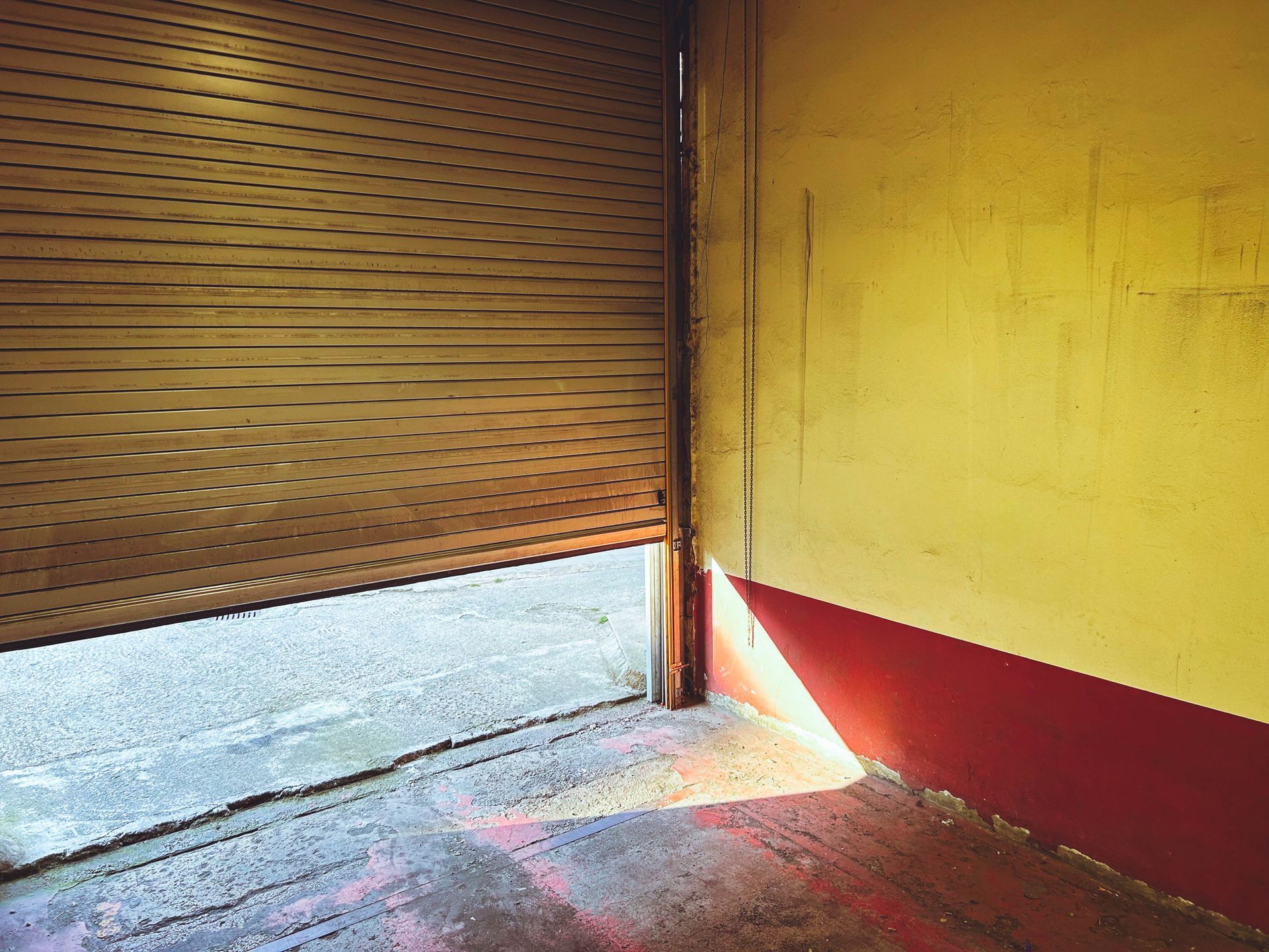 Partially open metal garage door casting a shadow on a red and yellow interior wall.