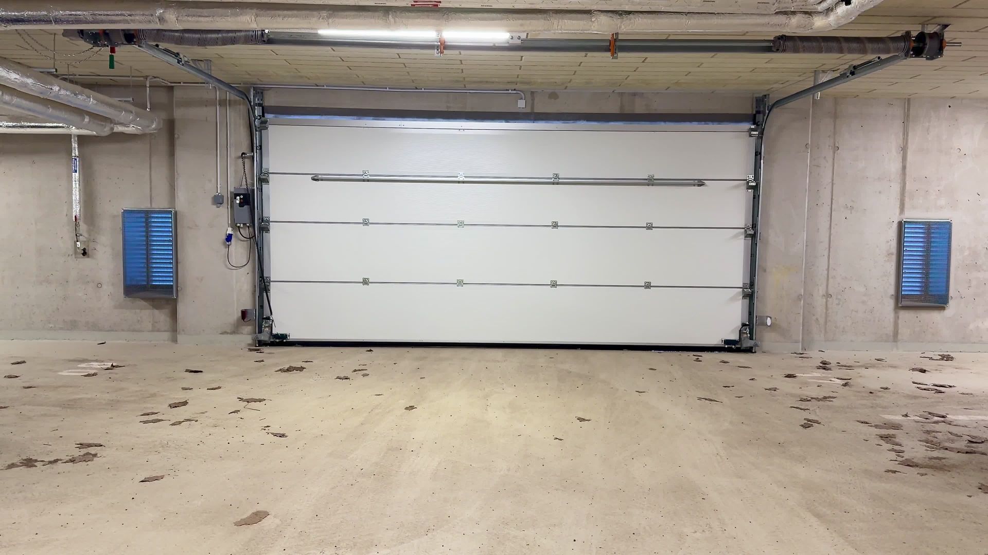 Garage door in a concrete room, two blue boxes on walls.