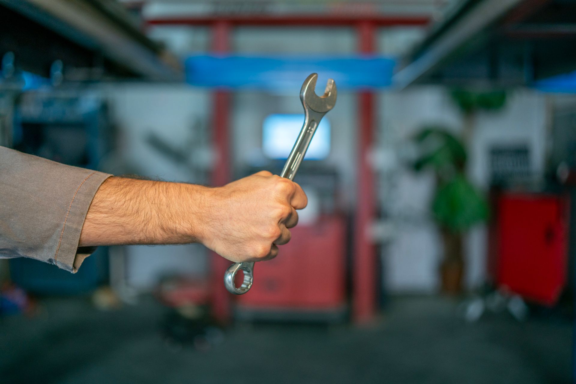 Hand holding wrench in a garage, blurred background of machinery and tools.