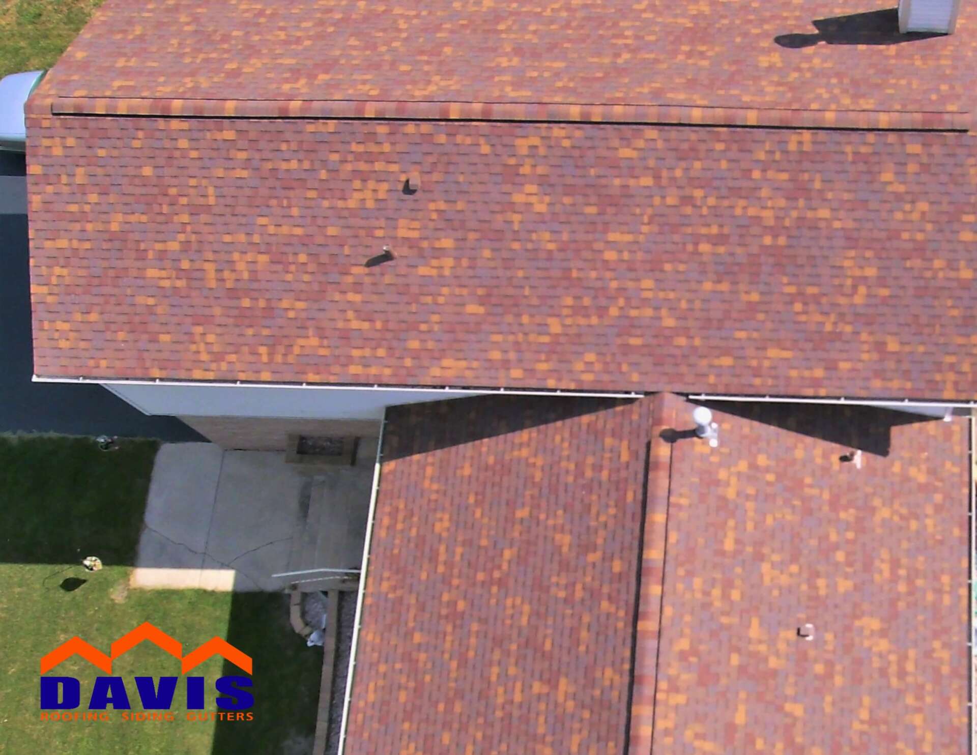 Overhead view of a residential roof with brown and orange shingles. A lawn and part of the house is visible.
