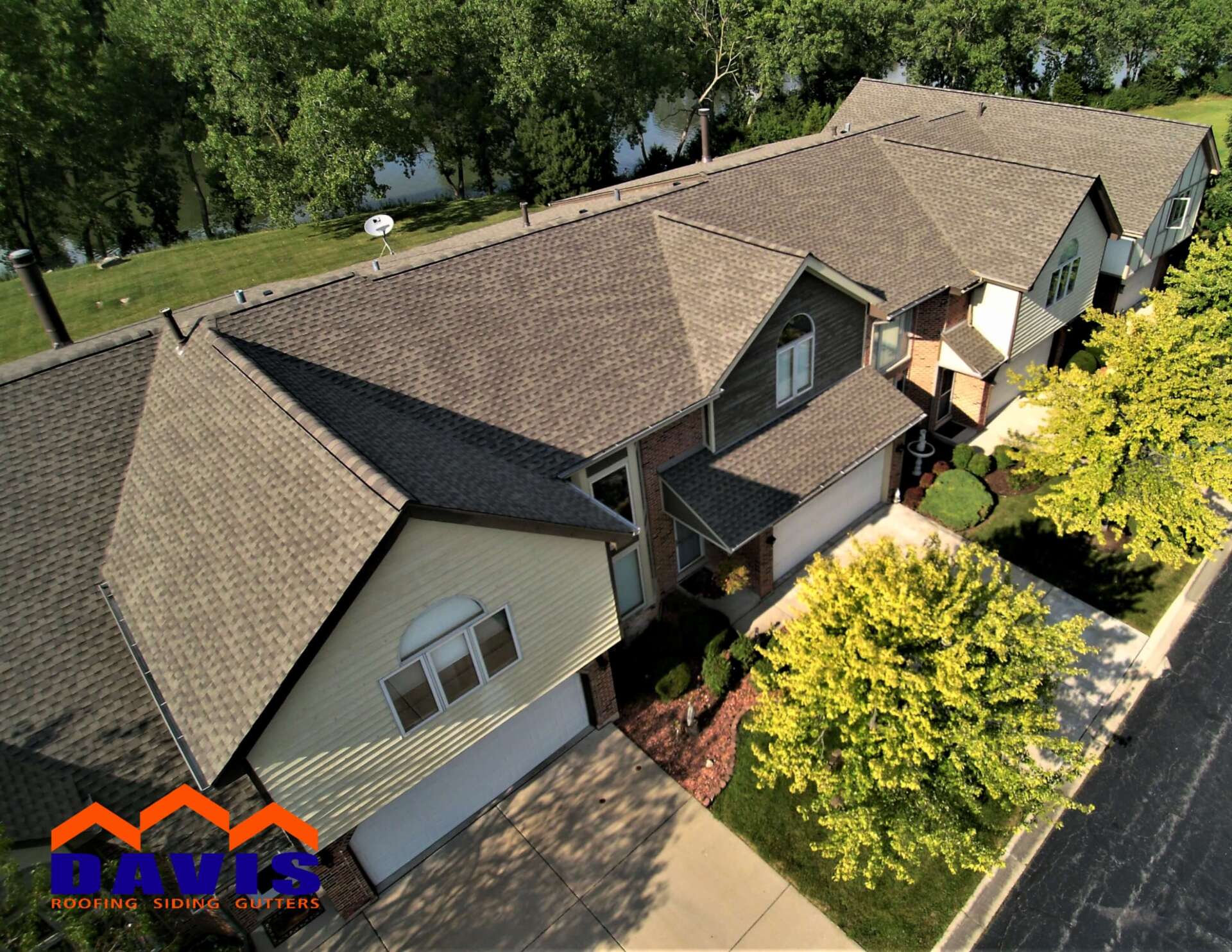 Aerial view of townhouses with brown roofs and beige siding, trees, and driveway.