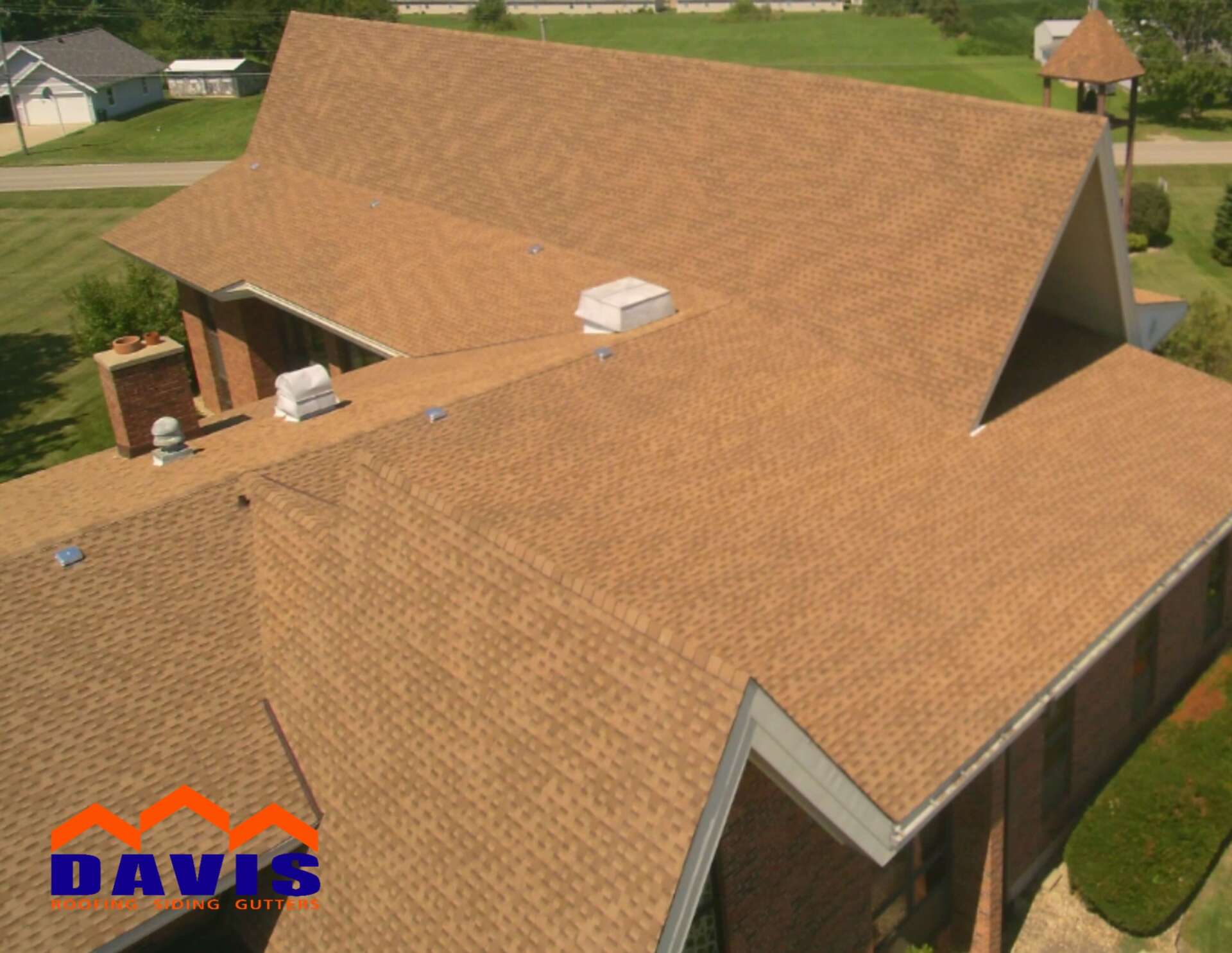 Brown shingle roof on a church building, aerial view. Davis Roofing logo in the corner.