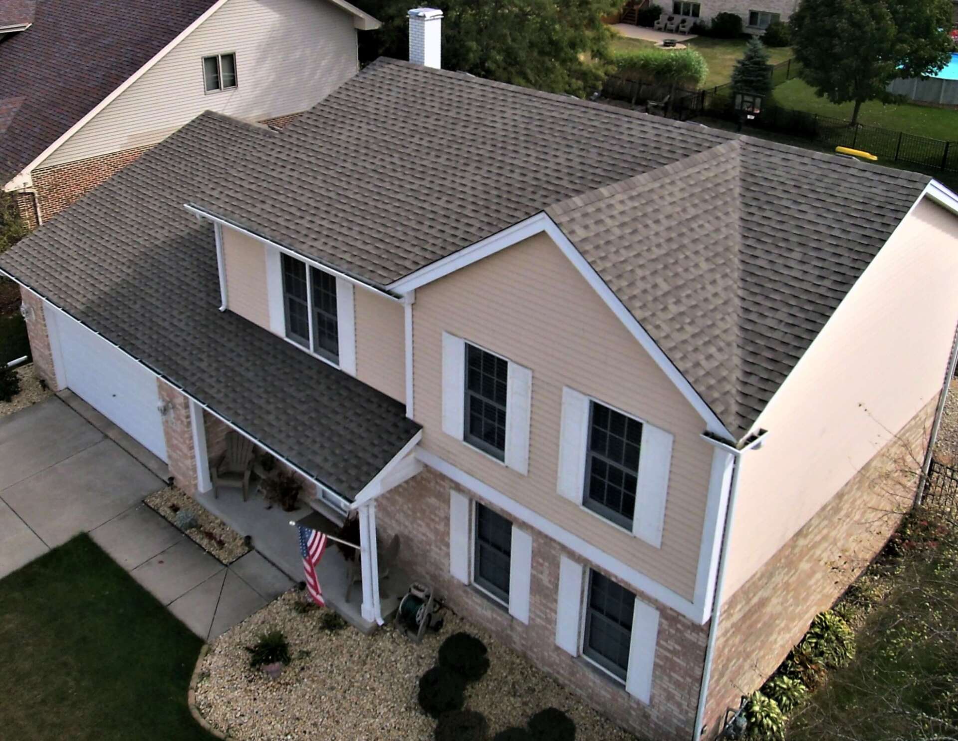 Aerial view of a two-story beige house with a dark gray roof, white trim, and a green lawn.