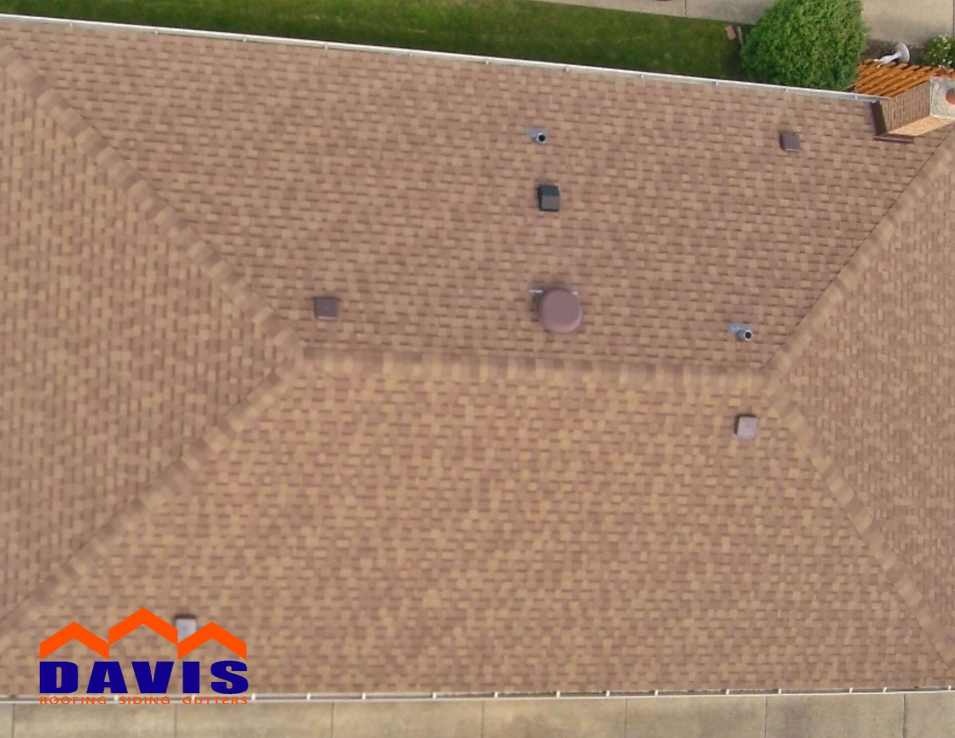 Overhead view of a brown shingle roof with vents and a chimney, from Davis Roofing.