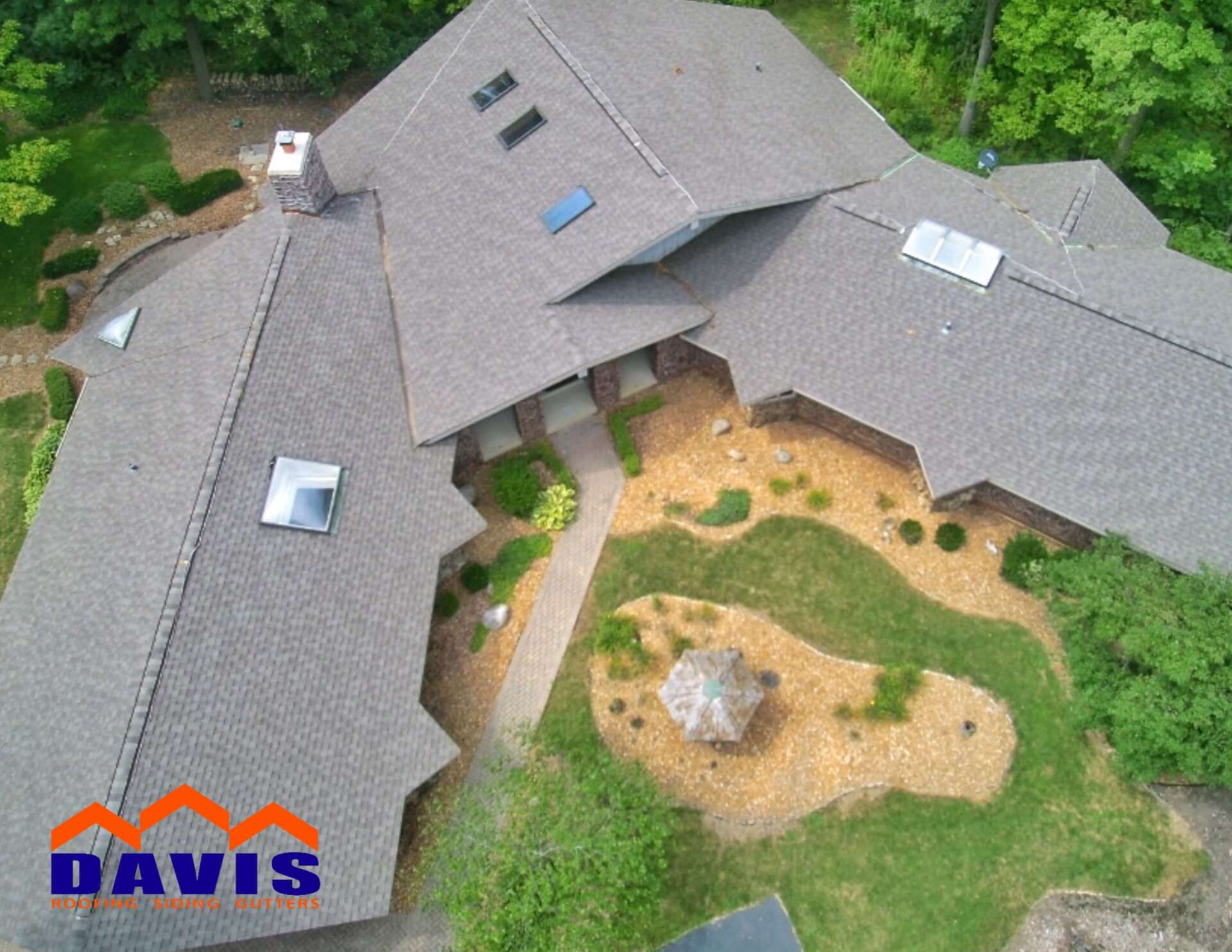 Aerial view of a house with a complex roof, a stone walkway, and landscaping.