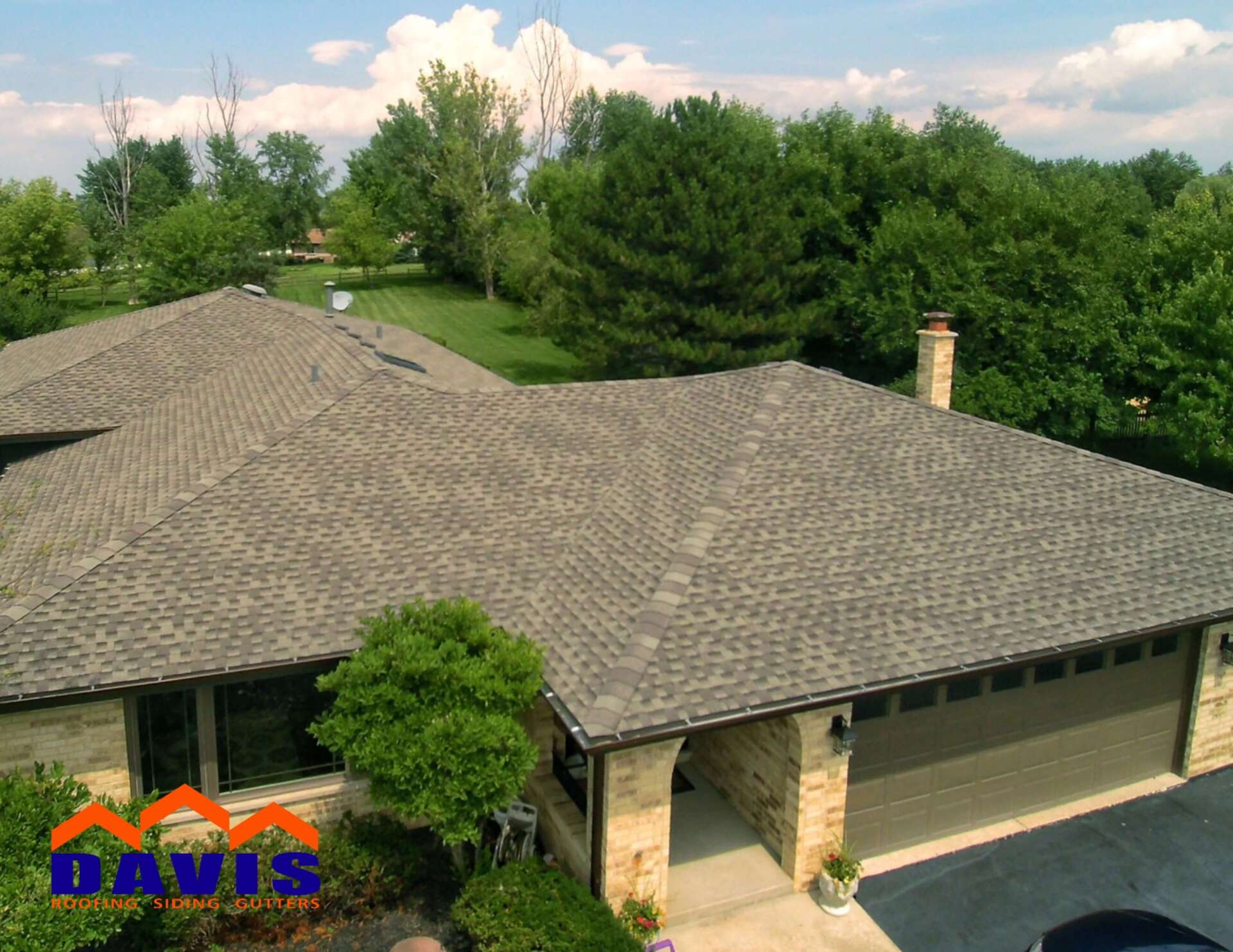 Overhead view of a house with a new brown shingle roof, green lawn, and trees.