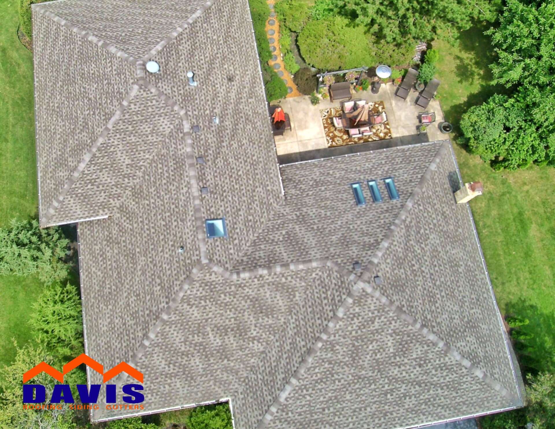 Overhead view of a residential roof with a patio and green yard.