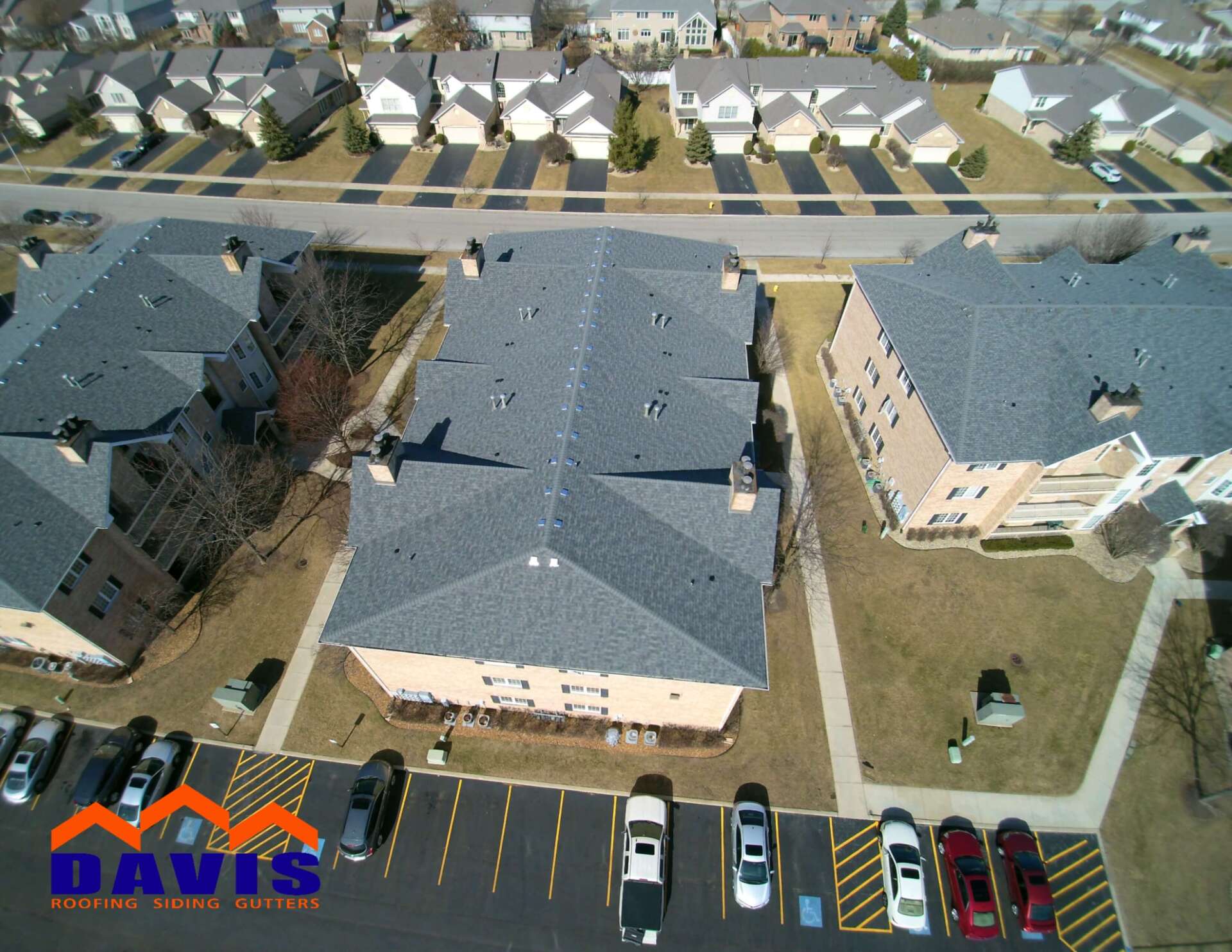 Aerial view of three buildings with gray rooftops, surrounded by parking and a neighborhood.