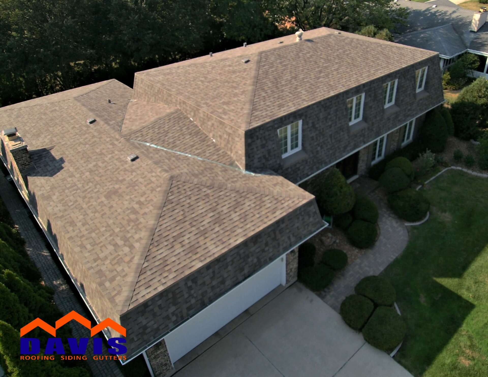 A house with a newly shingled roof. Gray shingles, white trim, garage door, and green lawn.
