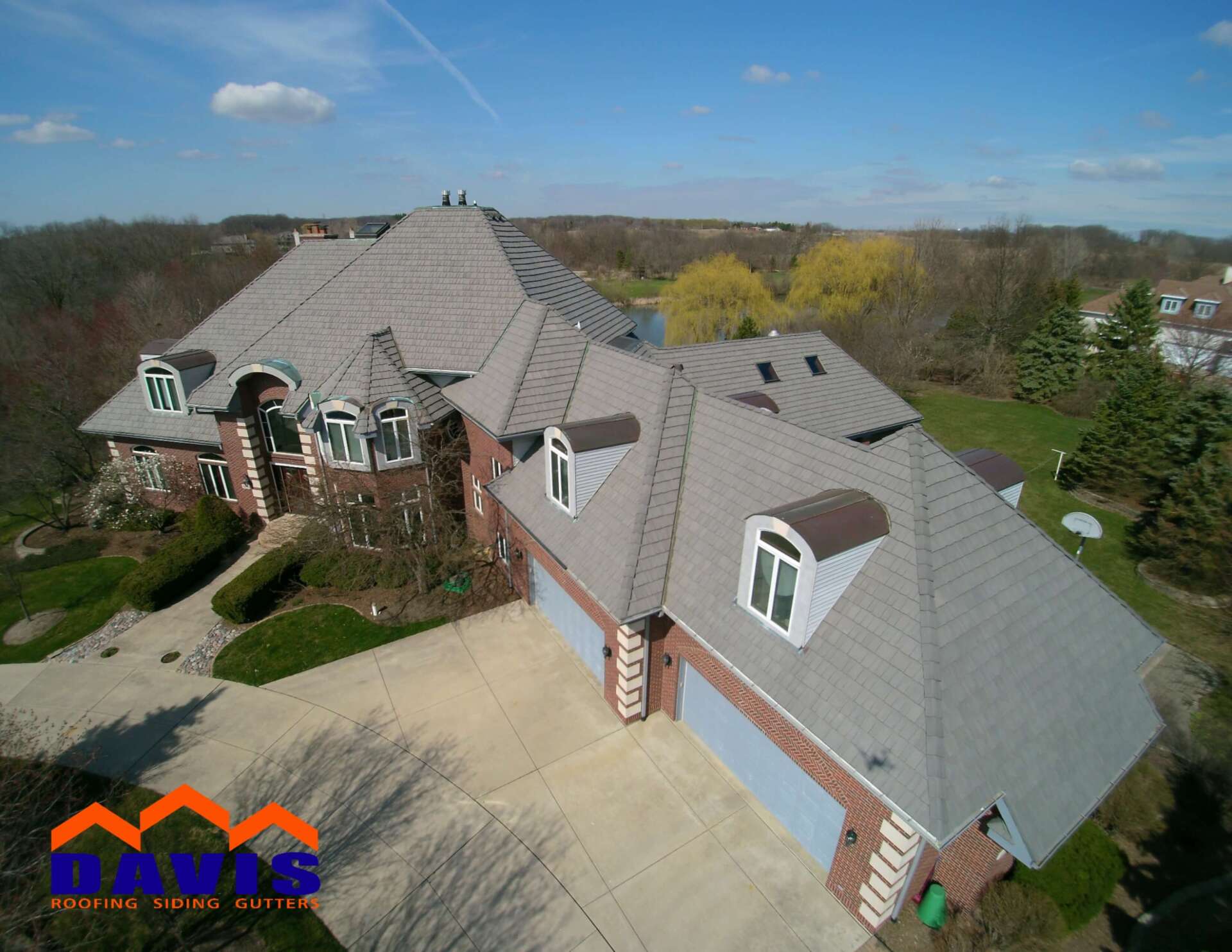 Aerial view of a large house with a gray roof, brick accents, and a long driveway.