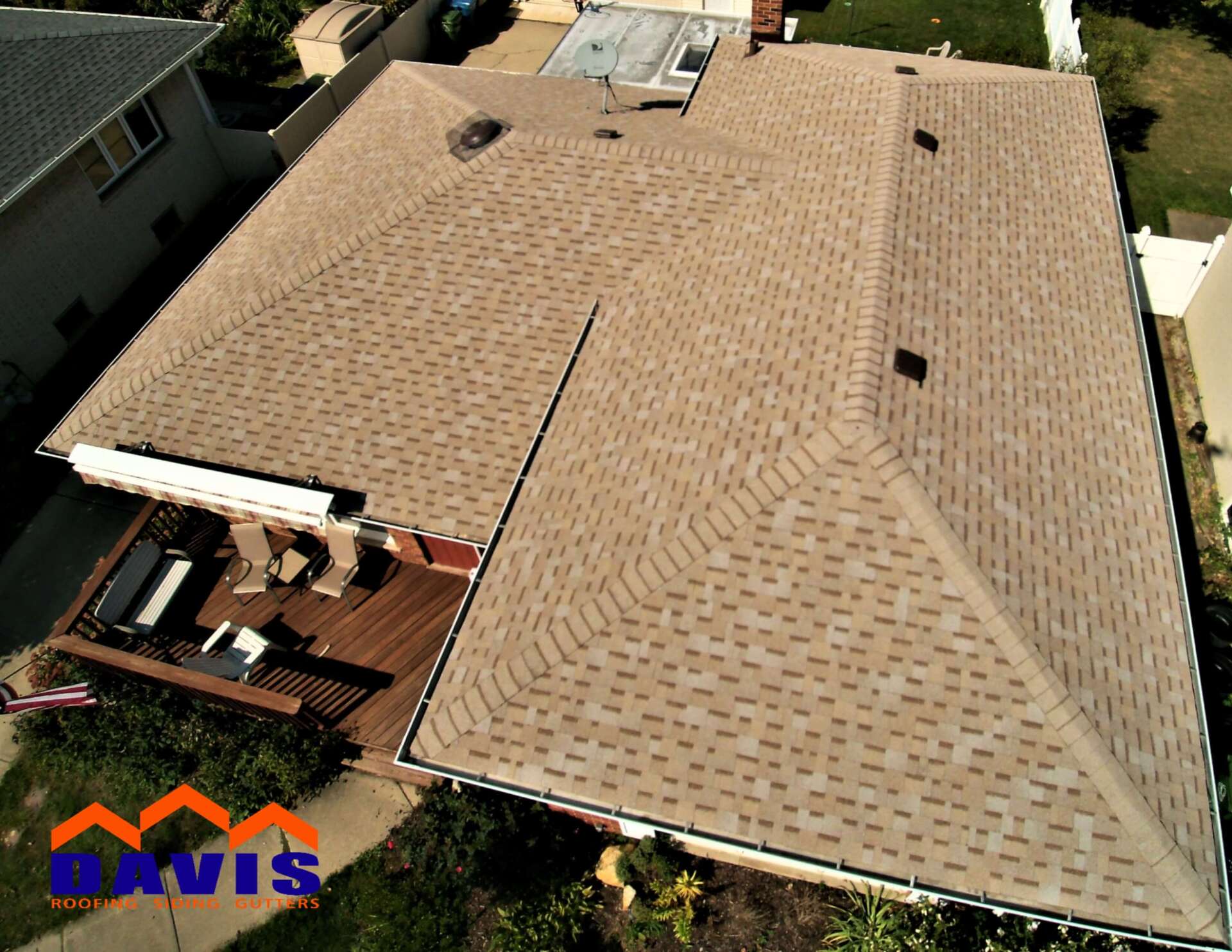 Aerial view of a house with a brown shingle roof, wooden deck, and green landscaping.