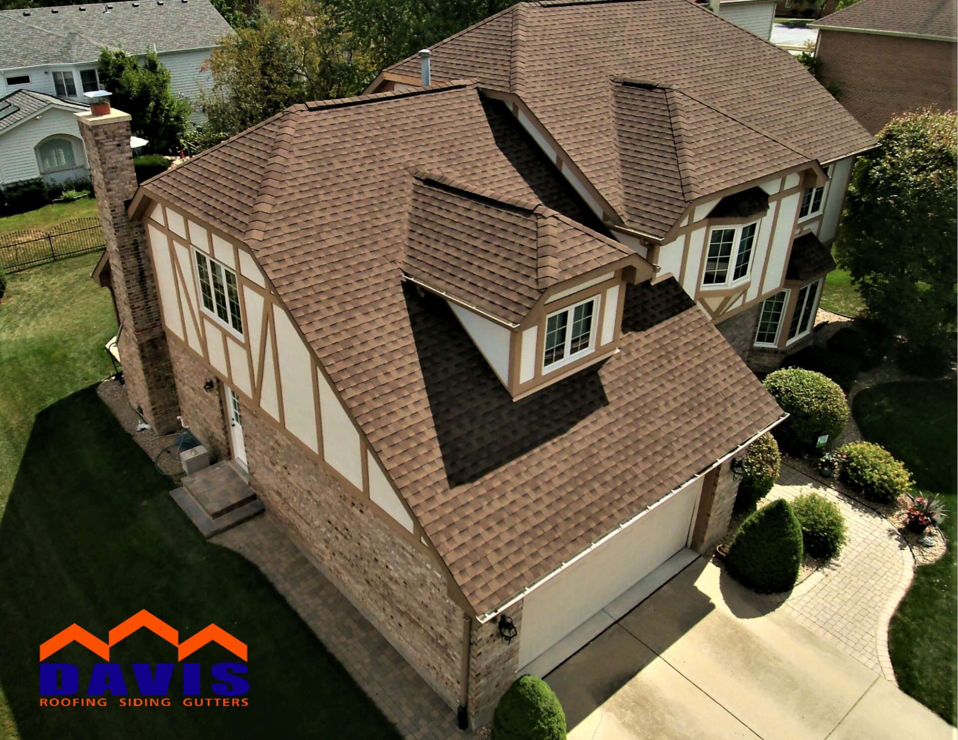 Brown-roofed house with Tudor-style design, brick and cream-colored siding. Includes a chimney, garage, and landscaping.