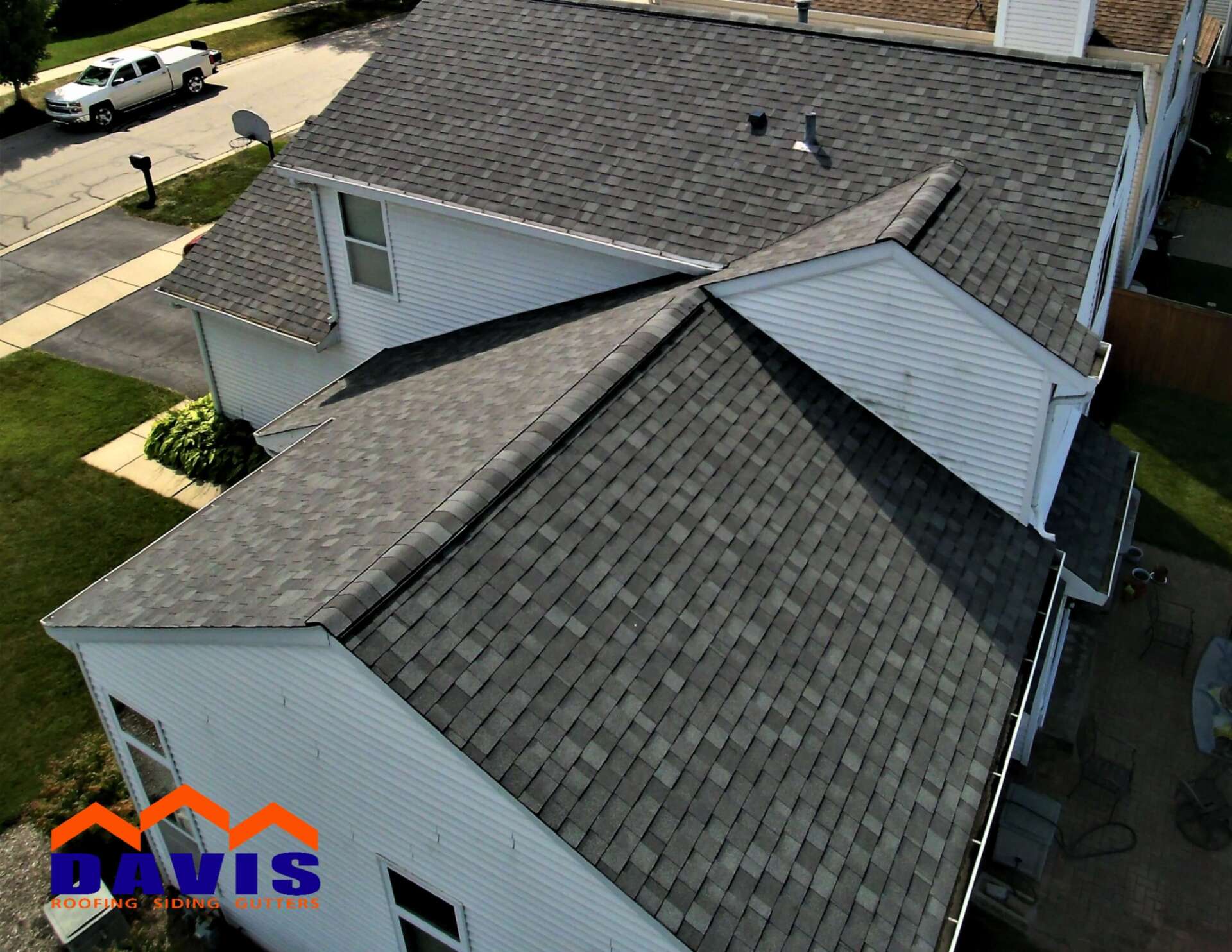 View of a house roof with gray shingles, white siding, and a surrounding green lawn.