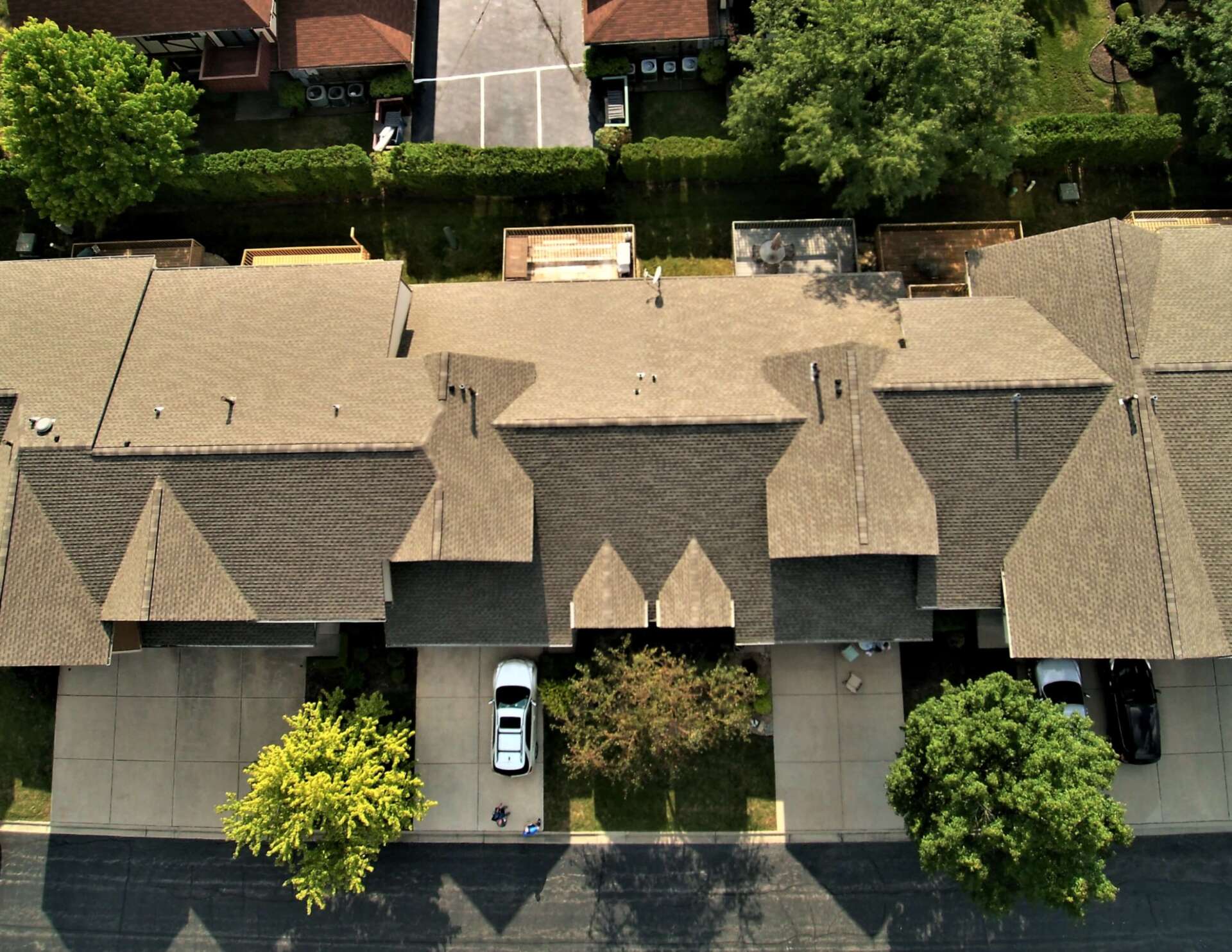 Aerial view of townhouses with tan roofs, driveways, parked cars, and trees.