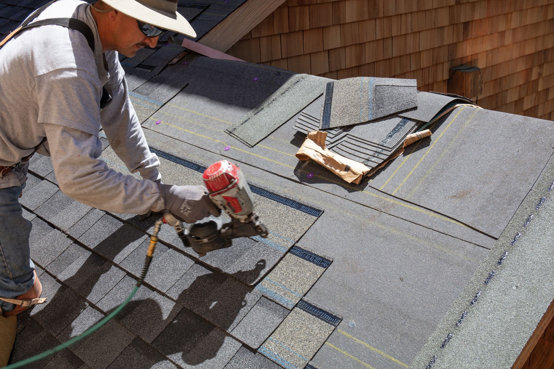 A man installing a new roof with a nail gun and shingles A man installing a new roof with a nail gun and shingles