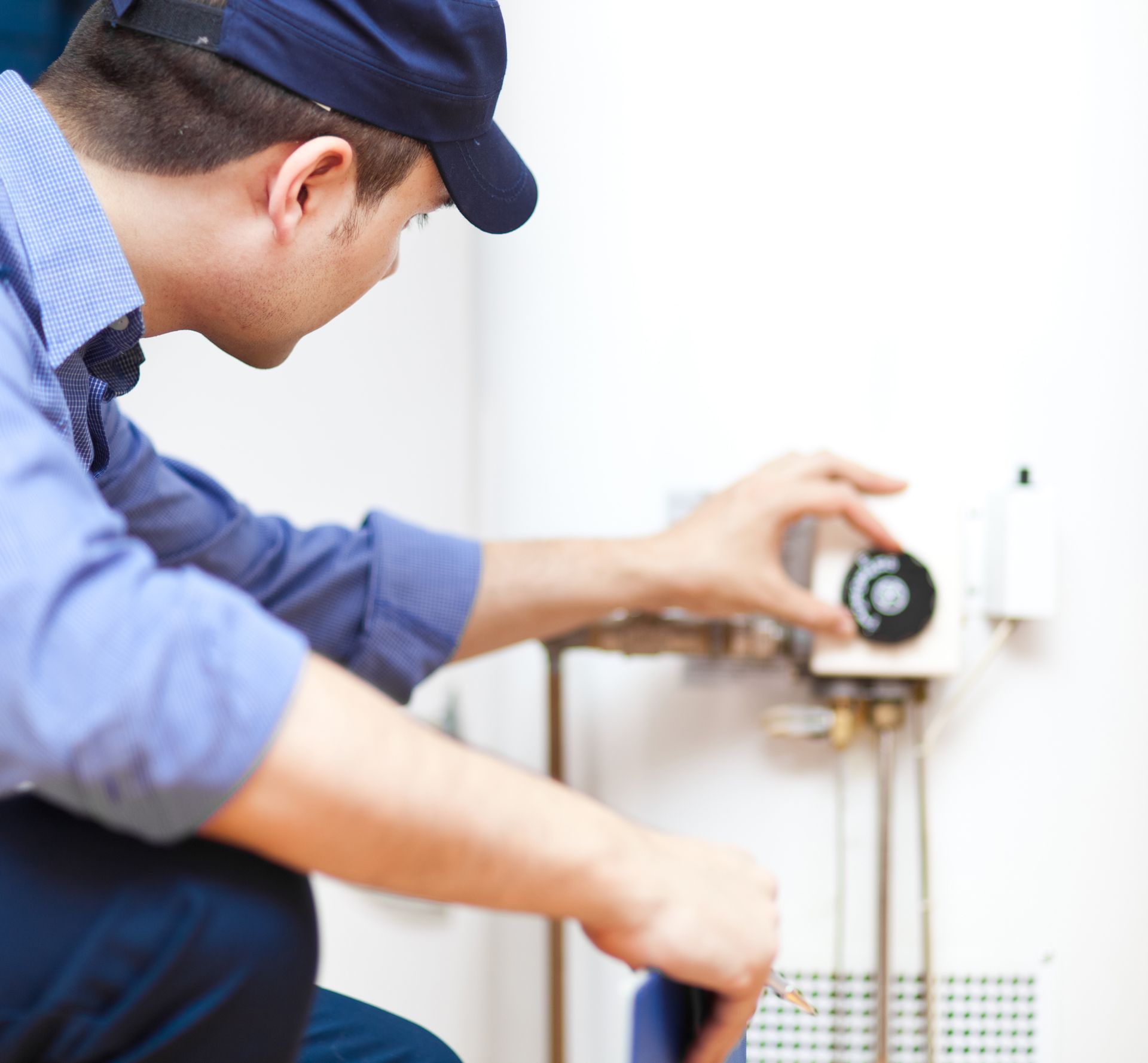 A man wearing a hat is working on a water heater