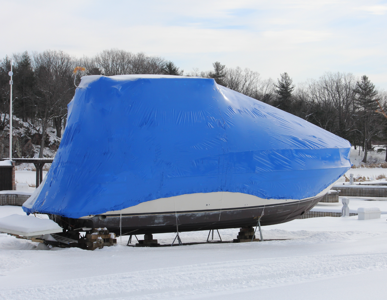 A blue tarp is covering a boat in the snow