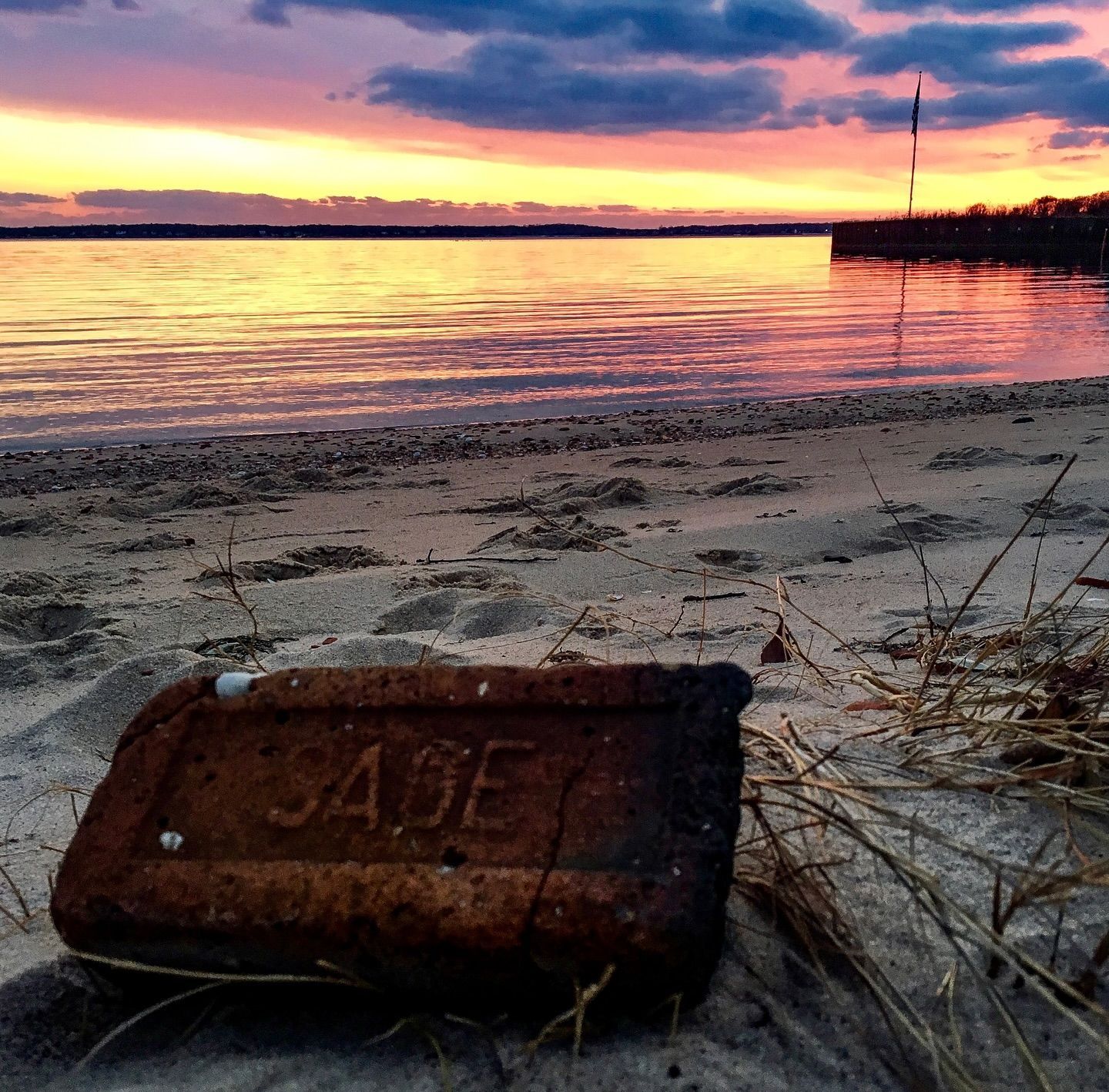 Sunset over calm water, with an old brick on a sandy beach; text