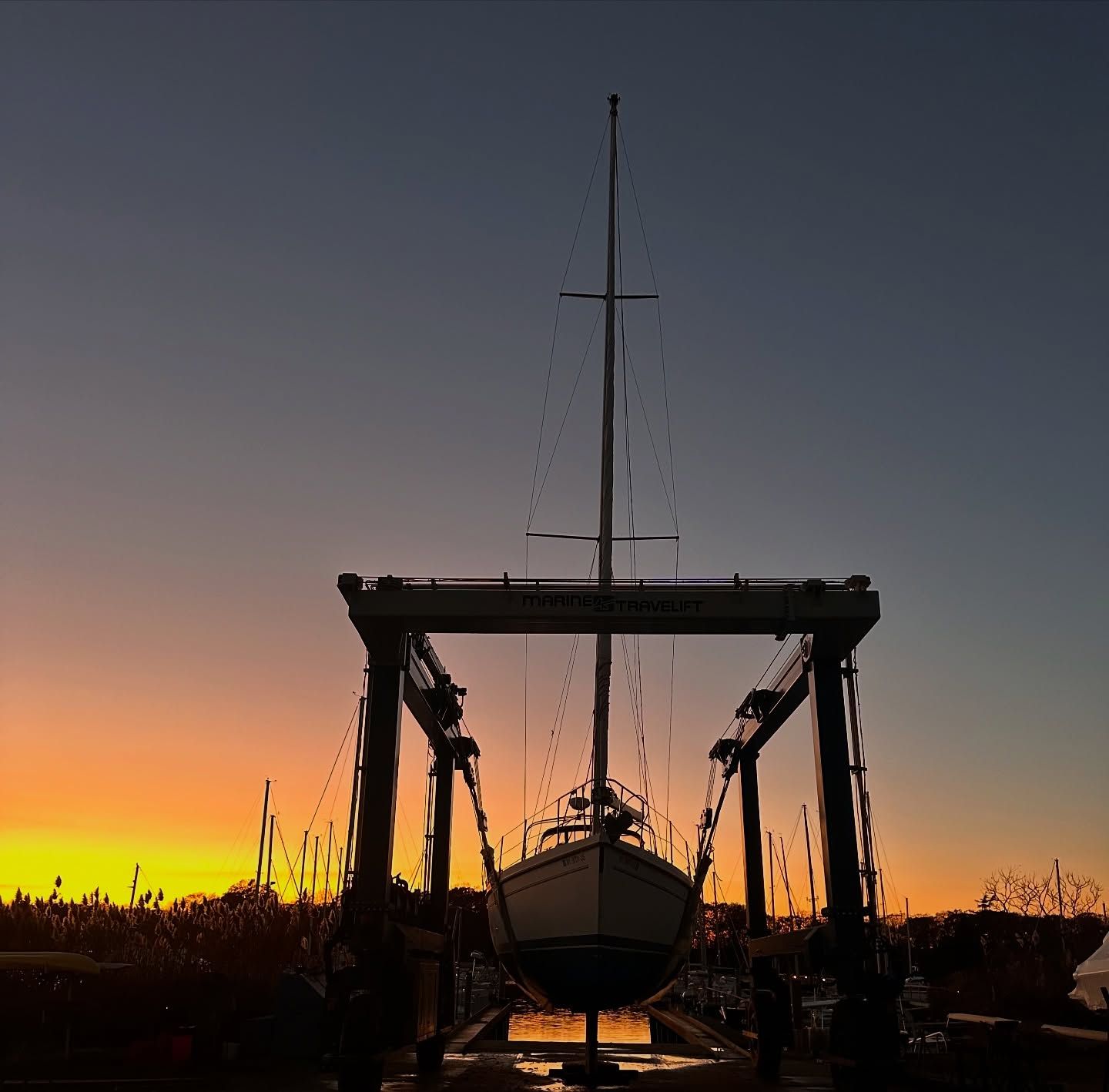 Sailboat suspended in lift against a vibrant sunset sky.