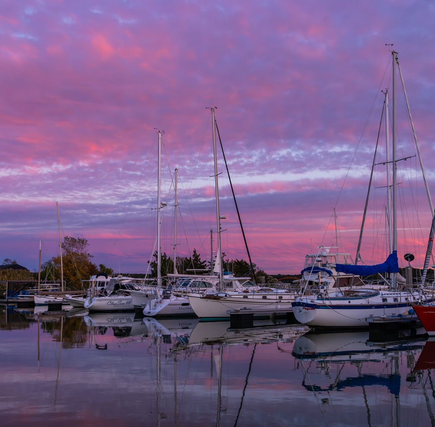 Sailboats docked in a harbor under a vibrant pink and purple sunset sky.
